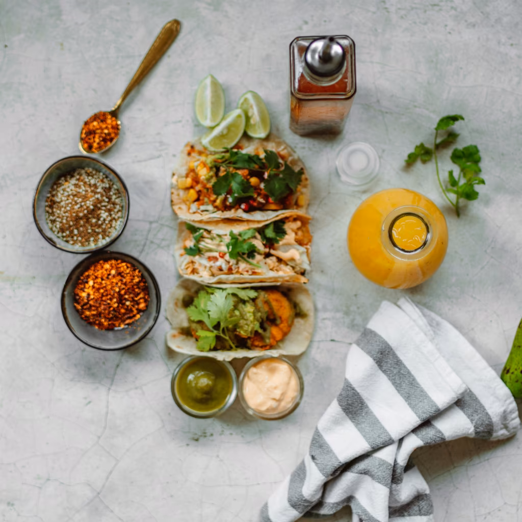 Petit bol de mélange d’épices pour tacos réalisé au Thermomix avec poudre rouge orangée entourée de paprika, cumin et piment sur une table de cuisine.